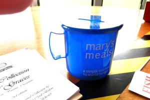 A blue cup-shaped collecting box next to a Rotary book of graces.